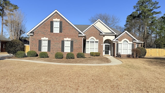 traditional-style house featuring fence, a front lawn, and brick siding