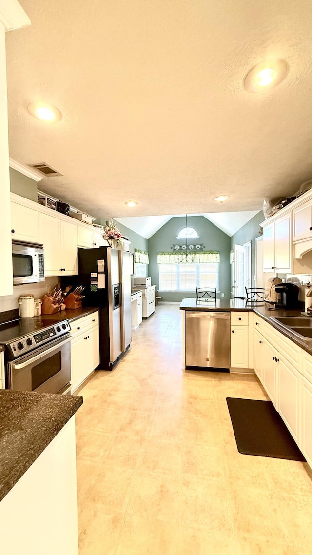 kitchen with stainless steel appliances, dark countertops, lofted ceiling, visible vents, and a sink