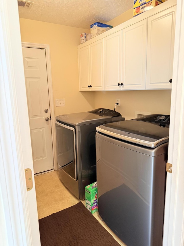 clothes washing area featuring cabinet space, washer and clothes dryer, and a textured ceiling