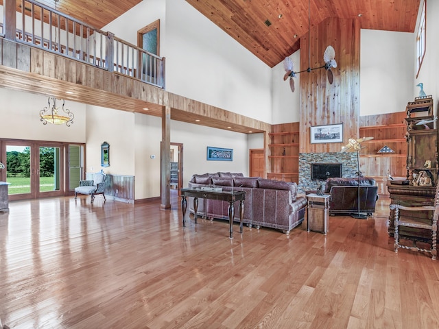 living room with light hardwood / wood-style floors, high vaulted ceiling, wooden ceiling, and a stone fireplace