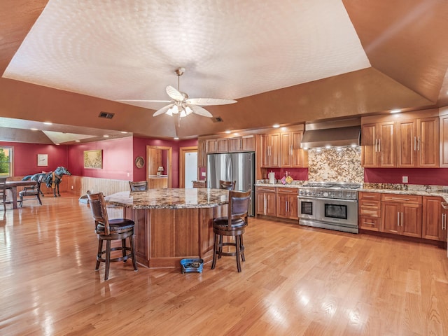 kitchen with wall chimney exhaust hood, stainless steel appliances, backsplash, lofted ceiling, and a breakfast bar