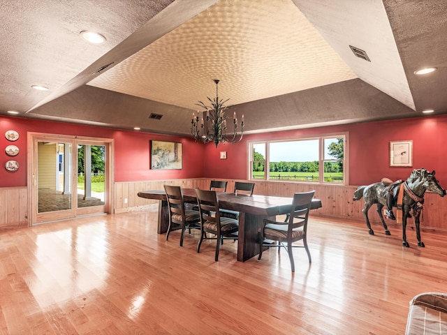 dining space with a tray ceiling, light wood-type flooring, a textured ceiling, and an inviting chandelier