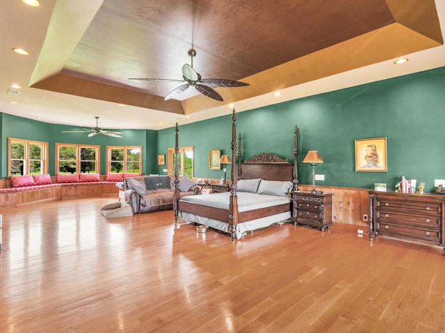 bedroom featuring ceiling fan, light wood-type flooring, and a tray ceiling