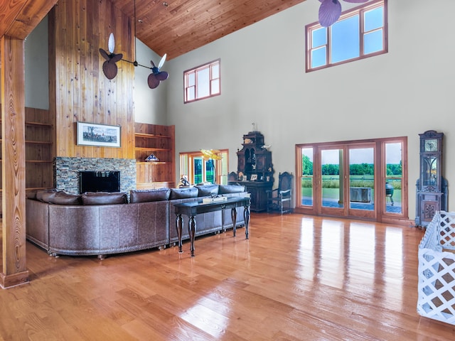 living room featuring hardwood / wood-style floors, high vaulted ceiling, wooden ceiling, and a stone fireplace