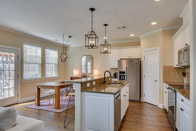 kitchen with sink, appliances with stainless steel finishes, a kitchen island with sink, white cabinets, and a kitchen bar