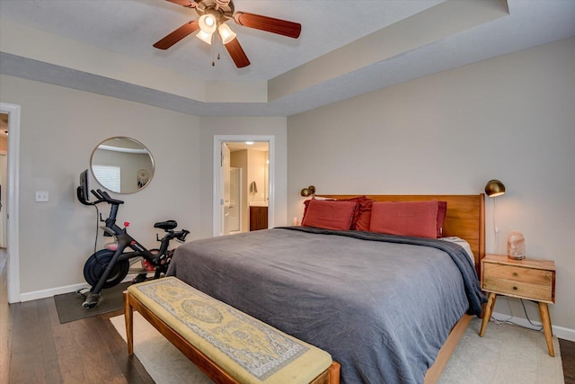 bedroom with a raised ceiling, ensuite bathroom, dark hardwood / wood-style floors, and ceiling fan