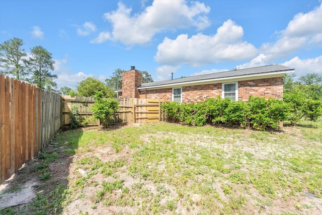 rear view of house featuring a fenced backyard, a chimney, and brick siding
