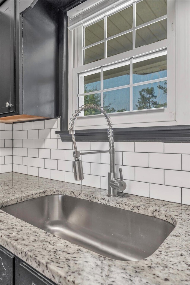 kitchen view of a sink, decorative backsplash, light stone counters, and dark cabinetry