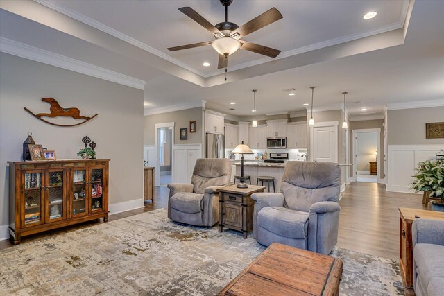 living room with ceiling fan, light wood-type flooring, and ornamental molding