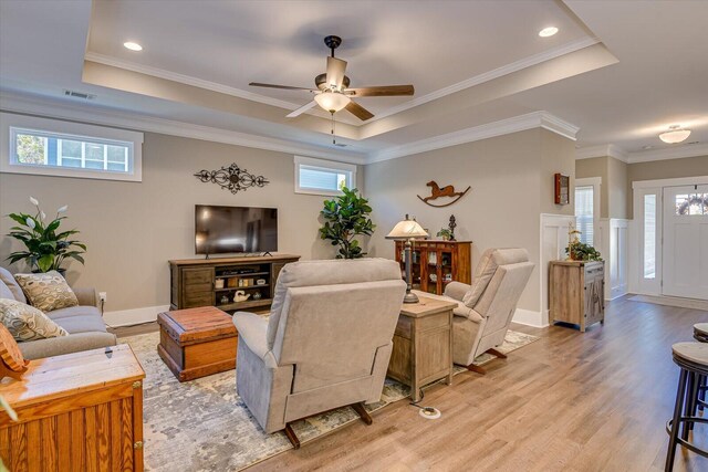 living room featuring light wood-type flooring, a tray ceiling, ceiling fan, and crown molding