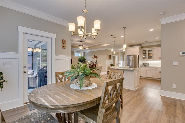 dining space featuring light wood-type flooring, ceiling fan with notable chandelier, ornamental molding, and sink