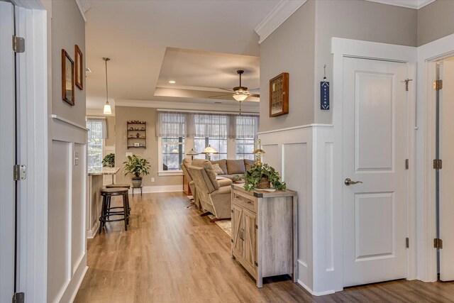 hall with a tray ceiling, crown molding, and light hardwood / wood-style flooring