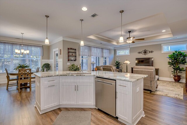 kitchen with white cabinets, a raised ceiling, stainless steel dishwasher, and an island with sink