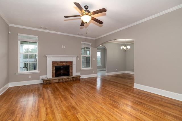 unfurnished living room featuring hardwood / wood-style flooring, ceiling fan with notable chandelier, a stone fireplace, and ornamental molding