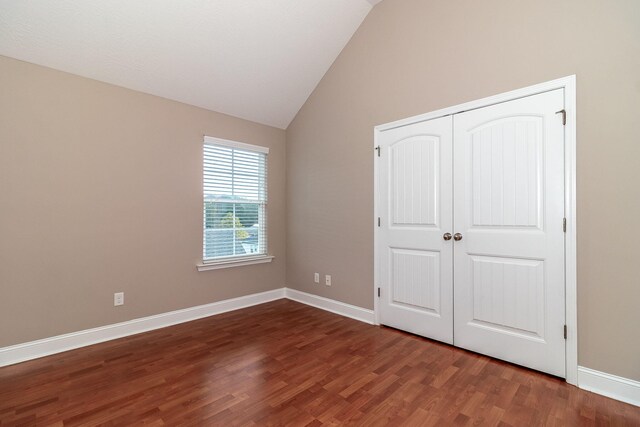 unfurnished bedroom with a closet, dark hardwood / wood-style flooring, and lofted ceiling