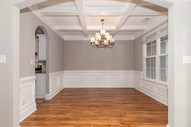 unfurnished dining area featuring hardwood / wood-style floors, ornamental molding, a notable chandelier, and beam ceiling