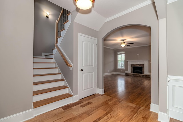 staircase with vaulted ceiling, hardwood / wood-style flooring, ceiling fan, ornamental molding, and a fireplace