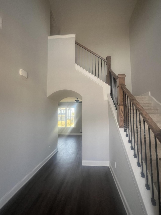 stairs with arched walkways, wood finished floors, a towering ceiling, and baseboards