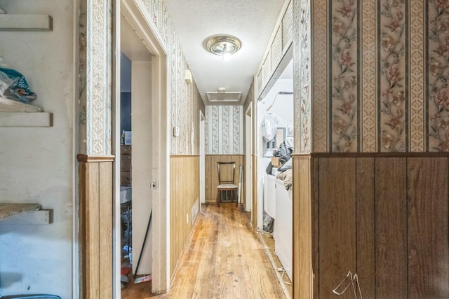 hallway with wallpapered walls, wood finished floors, a textured ceiling, and a wainscoted wall