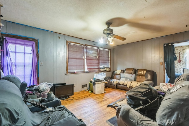 living room with wood walls, a ceiling fan, wood finished floors, and a textured ceiling