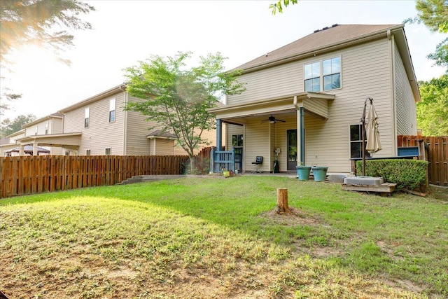 rear view of property featuring ceiling fan and a yard