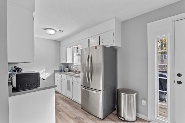 kitchen with white cabinets, plenty of natural light, stainless steel fridge, and sink