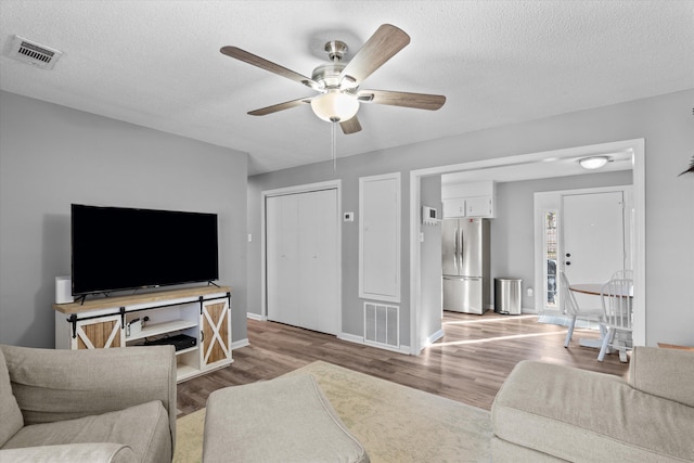 living room with ceiling fan, a textured ceiling, and light hardwood / wood-style flooring