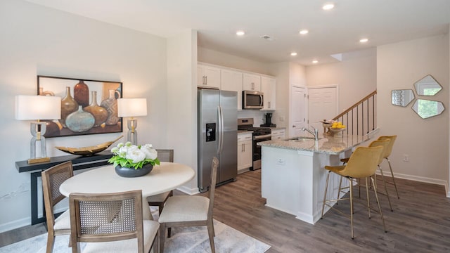 kitchen featuring light stone counters, dark wood-style flooring, a center island with sink, appliances with stainless steel finishes, and white cabinets