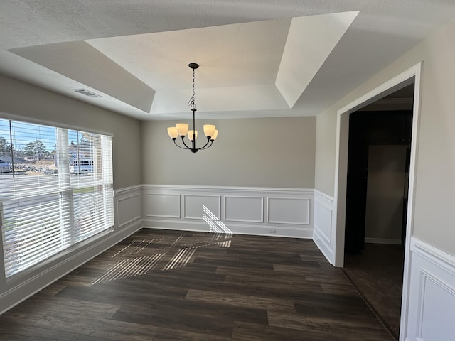 unfurnished dining area with a notable chandelier, dark wood-type flooring, and a raised ceiling