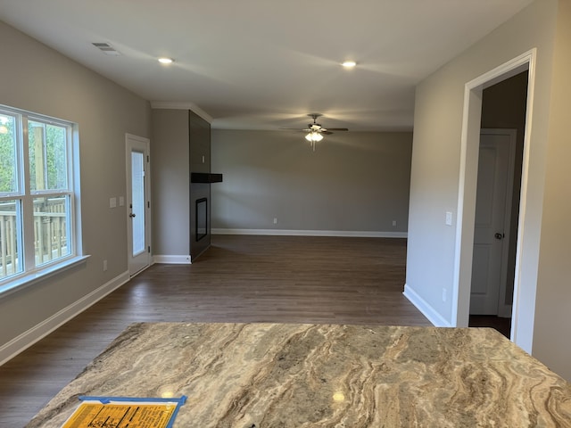 unfurnished living room with baseboards, a glass covered fireplace, dark wood-type flooring, and ceiling fan
