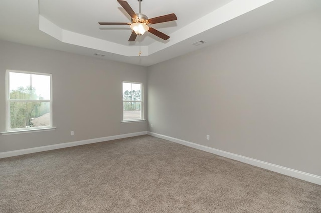 carpeted spare room with ceiling fan, a wealth of natural light, and a tray ceiling