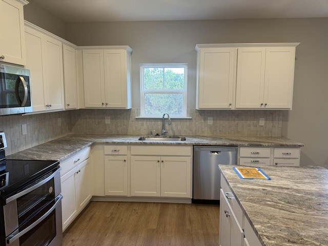 kitchen with light stone counters, wood finished floors, a sink, white cabinets, and appliances with stainless steel finishes