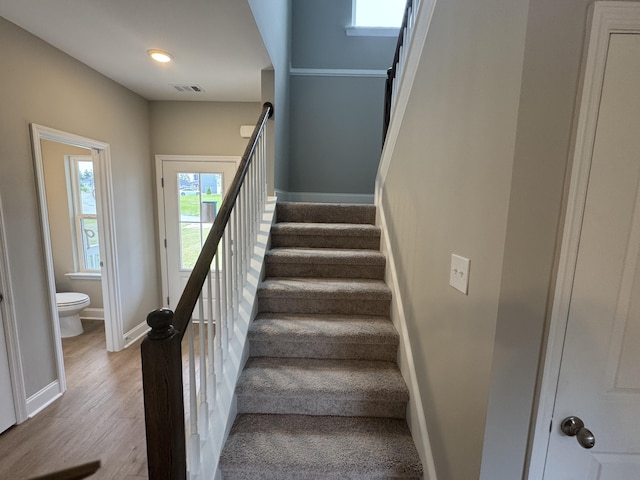 stairs with baseboards, wood finished floors, and visible vents