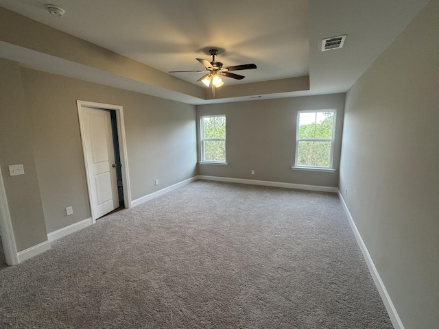 carpeted empty room featuring a tray ceiling, visible vents, a ceiling fan, and baseboards