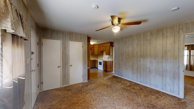 interior space with wood walls, a ceiling fan, and dark colored carpet