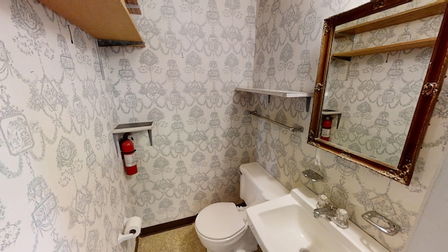 half bathroom featuring wallpapered walls, toilet, baseboards, and a sink