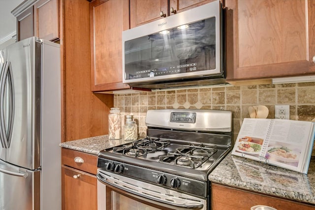 kitchen featuring stainless steel appliances, brown cabinets, tasteful backsplash, and light stone countertops