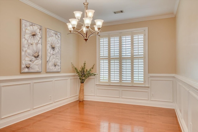 spare room featuring visible vents, light wood-style flooring, ornamental molding, a decorative wall, and a chandelier