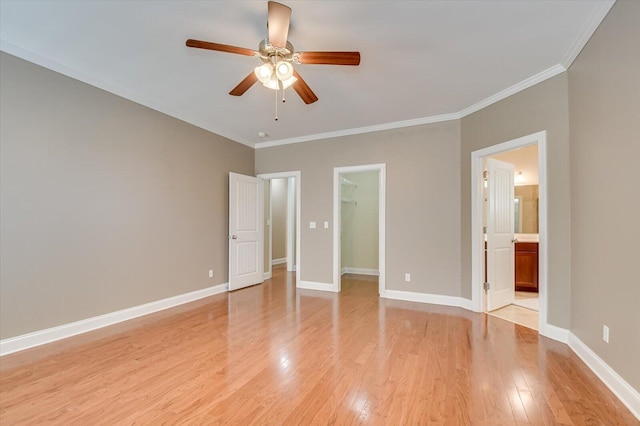 unfurnished bedroom featuring a walk in closet, light wood-style flooring, baseboards, and ornamental molding