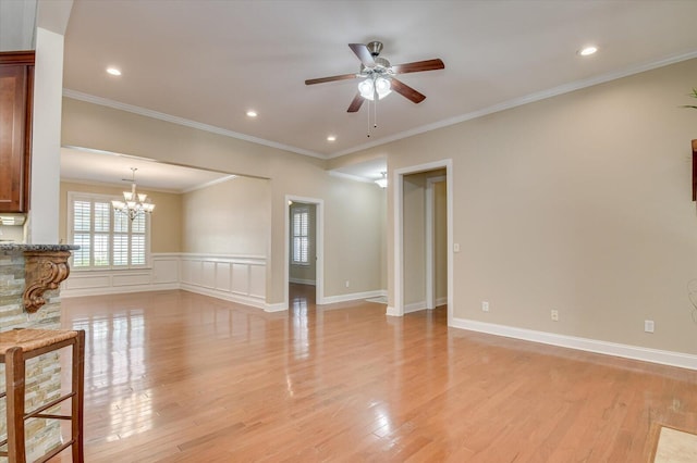 unfurnished living room with a wainscoted wall, recessed lighting, ornamental molding, ceiling fan with notable chandelier, and light wood-type flooring