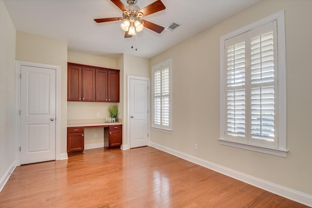 interior space featuring ceiling fan, baseboards, light wood-style flooring, and built in study area