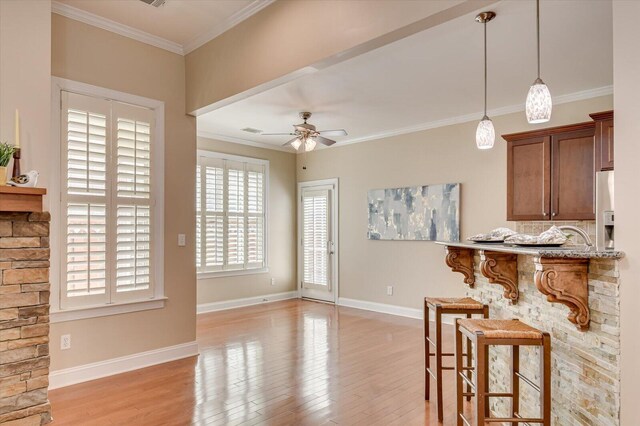 kitchen with a kitchen bar, crown molding, a ceiling fan, and light wood-style floors