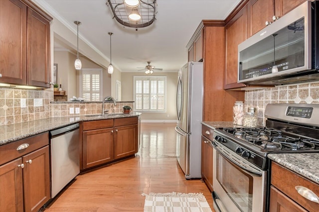 kitchen with a peninsula, a sink, stainless steel appliances, crown molding, and brown cabinets