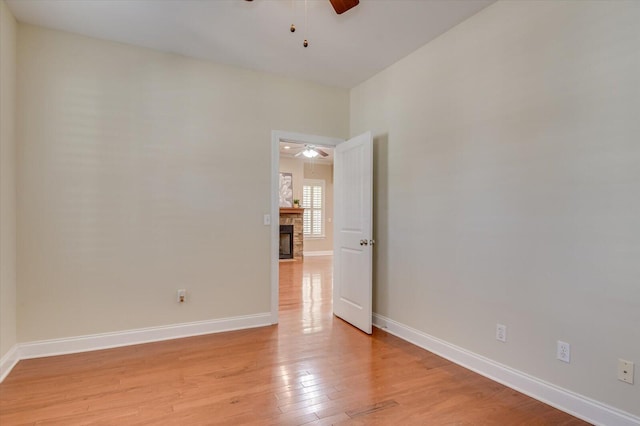 empty room featuring light wood-style flooring, a fireplace, baseboards, and ceiling fan