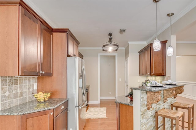 kitchen featuring light wood finished floors, stainless steel fridge, stone countertops, and a peninsula