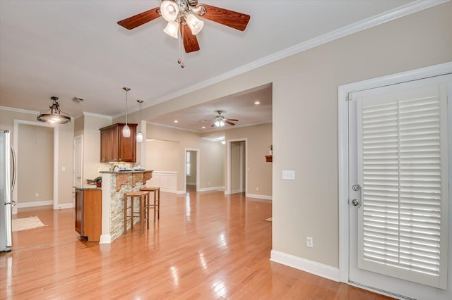 kitchen with a breakfast bar area, brown cabinetry, light wood finished floors, freestanding refrigerator, and crown molding