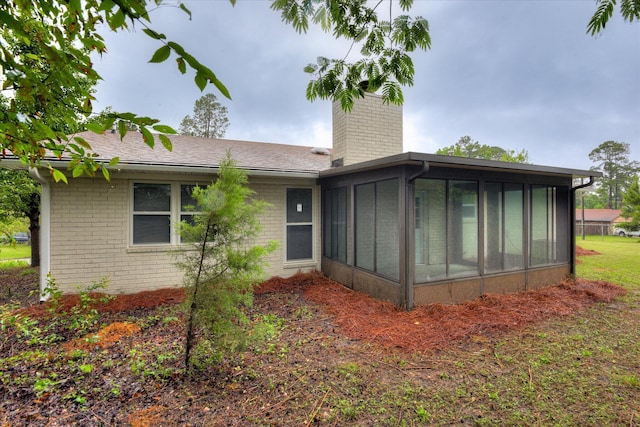 rear view of house featuring brick siding, a sunroom, a chimney, and roof with shingles