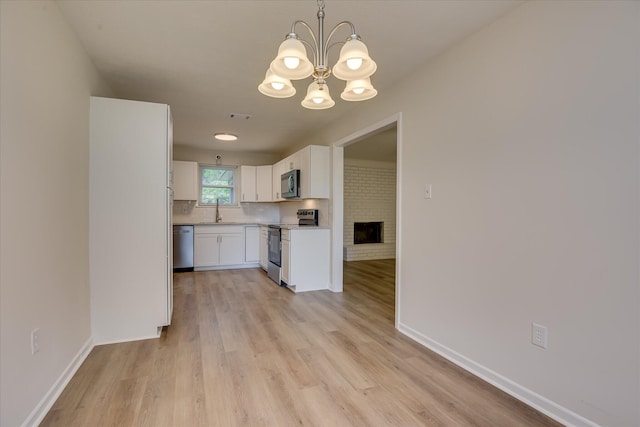 kitchen with stainless steel appliances, white cabinetry, a chandelier, light wood-style flooring, and baseboards