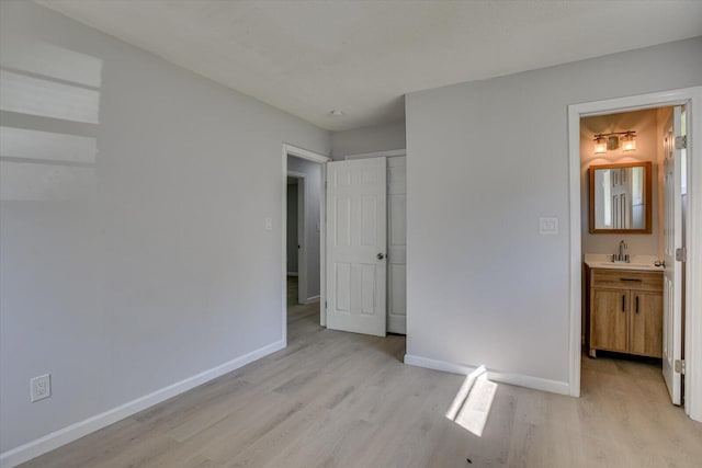 unfurnished bedroom featuring a closet, ensuite bathroom, sink, and light hardwood / wood-style flooring