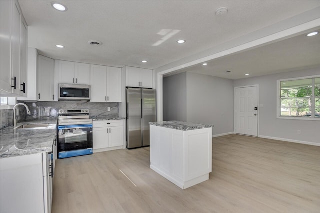 kitchen with sink, a kitchen island, light stone counters, white cabinets, and appliances with stainless steel finishes